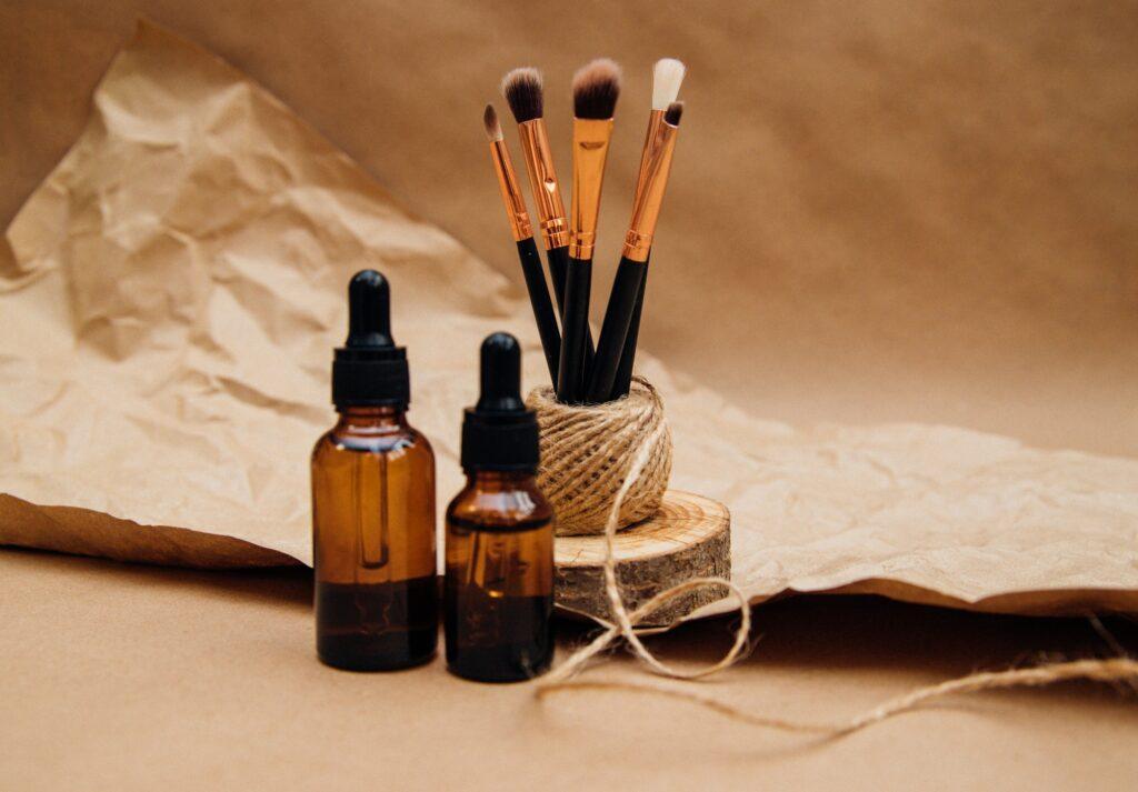 Cosmetic oil in a container with a pipette. Makeup brushes stand on a podium made of sawn wood.